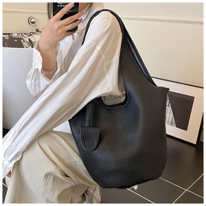 Detail of minimalist black pebbled leather bucket bag with matching leather clochette tag