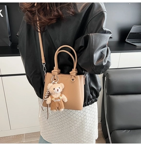 Detail of tan lychee texture handbag featuring a cute plush bear charm in an office setting
