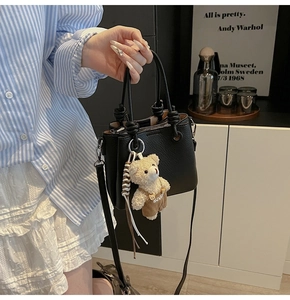 Detail of black pebbled leather bucket bag with cute bear charm and long crossbody strap