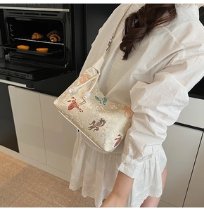 Detail of embroidered bird and cloud patterns on a cream hobo canvas shoulder bag