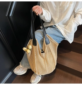 Détail d'un sac cabas en maille beige avec bandoulières en cuir noir sur un escalier