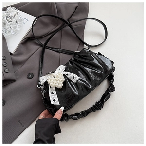 Detailed close-up of a black glossy pleated shoulder bag featuring a lace pearl bow