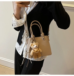 Close-up of beige lychee texture bucket bag with cute bear charm and adjustable strap