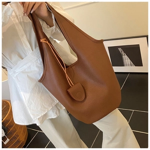 Detailed view of brown litchi grain leather bucket bag with buckle on a female model