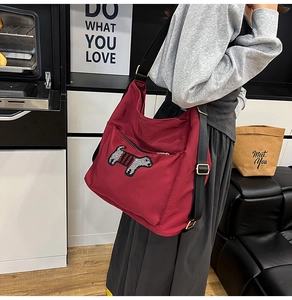 Detail of burgundy nylon crossbody bag with cute dog embroidery and adjustable strap