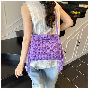 Detail of purple hand-knitted crossbody bag with bohemian tassels and woven shoulder strap