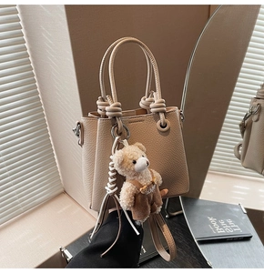 Detail of beige litchi grain bucket bag with a cute teddy bear charm and knotted handle