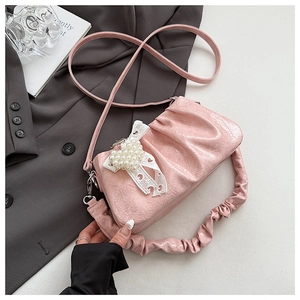 Macro detail of pink pleated handbag featuring pearl bow pendant and glossy leather texture