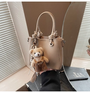 Detail of beige bucket bag with lychee texture and plush bear charm on a handle