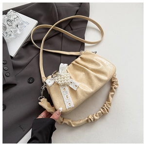 Detail of beige pleated shoulder bag with pearl bow charm on a grey suit jacket