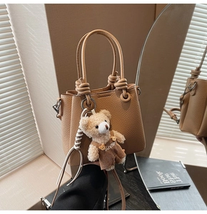 Close-up of camel lychee leather bucket bag with a cute bear charm and knotted handle