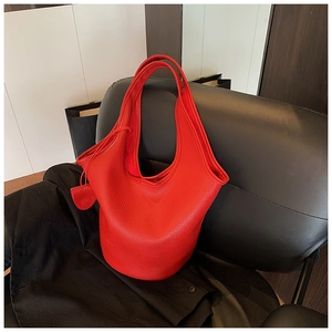 Detail of red pebbled leather texture and side tassel on a large capacity bucket bag