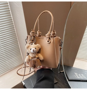 Close-up of camel lychee pattern leather handbag with knot handle and teddy bear charm
