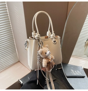 Close-up of cream textured leather bucket bag with knot handle and teddy bear charm