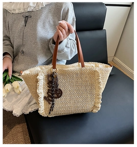 Detail of woven straw tote bag with herringbone pattern and brown leather handle
