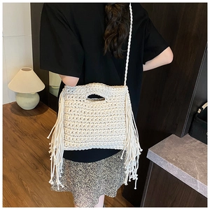 Detail of bohemian cream knit crossbody bag with long fringes shown on a model