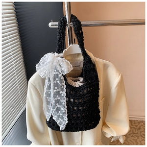 Close-up of black crochet knit bucket bag with white lace floral bow on beige blazer