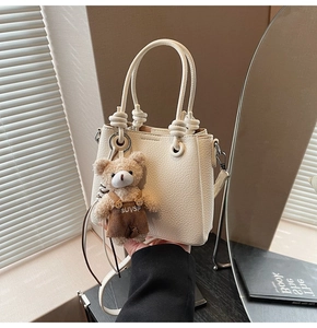 Detail of off-white lychee leather bucket bag featuring a knot handle and teddy bear charm