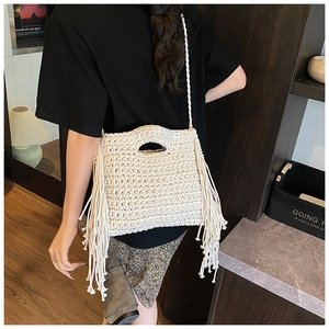 Detail view of cream white woven shoulder bag featuring long side tassels and thick knit texture