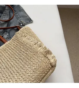 Close-up of handwoven straw tote bag with fringe edge and slim brown leather strap