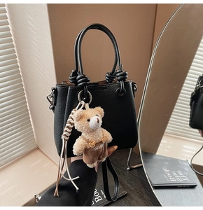 Detail of black lychee grain bucket bag with decorative knot handle and cute bear charm