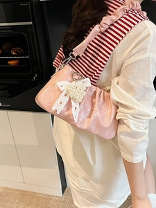 Pink pleated underarm bag with lace bow and pearl heart pendant on model in a kitchen