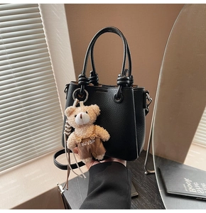 Detail view of black lychee leather mini bucket bag with bear charm and knot handles