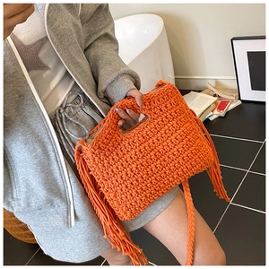 Detail of orange woven tote bag with fringe tassels and crossbody strap on a model