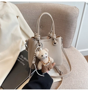 Detail view of beige lychee leather bucket bag with a cute plush bear charm on a sofa