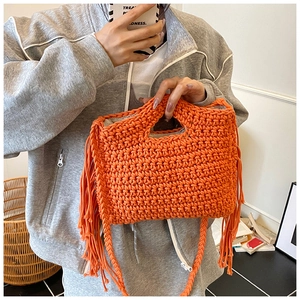 Close-up of bright orange knitted handbag featuring decorative fringe and woven texture