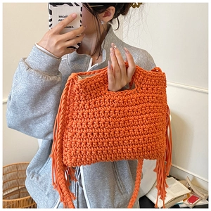 Close-up of orange hand-knitted crossbody bag with bohemian tassels and woven texture