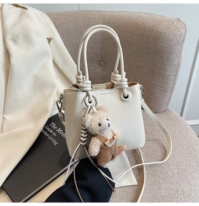 Detail of white lychee grain bucket bag with knot handle and cute bear charm accessory