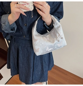Detail of embroidered butterfly handbag with bead charm and satin texture on denim outfit