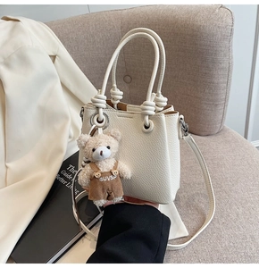 Detail of cream white pebbled leather bucket bag with knotted handles and a cute bear charm