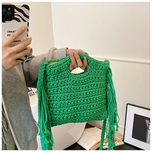 Detail of green crochet knit handbag with square frame and long tassel ornaments