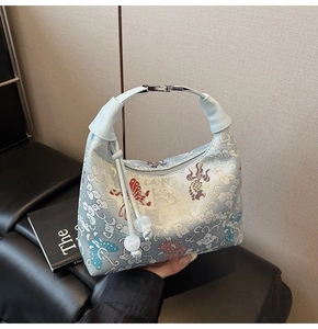 Detail of light blue embroidered canvas dumpling bag with fish motifs and beaded tassel