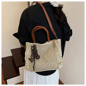 Detail of woven straw tote bag with brown leather handles and decorative ruffles