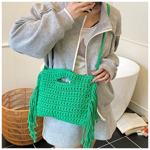 Detail of green hand-woven knit bag featuring long side tassels and thick cotton rope texture