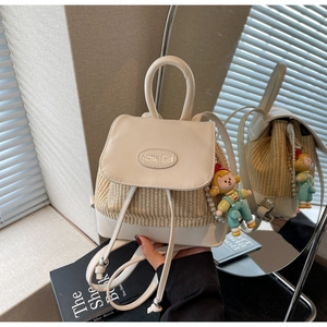 Detail des PU-Leder und Stroh-Rucksacks mit Acme Girl Metalllogo und einem süßen Puppenanhänger