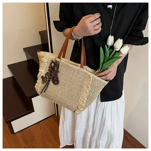 Close-up of woven straw tote bag featuring decorative fringe and brown leather handles