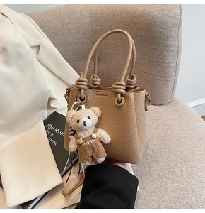 Detail of khaki pebbled leather handbag with knotted handle and plush bear charm
