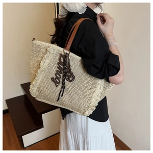 Detail of woven straw tote bag with brown leather handles and decorative boira charm