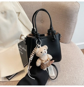 Close-up of black lychee leather bucket bag with knot handle and teddy bear charm