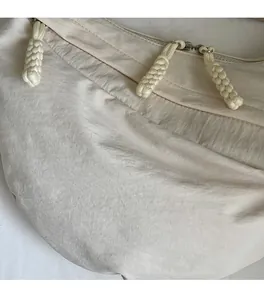 Detail of cream nylon fabric texture and braided rope zipper pulls on the crossbody bag