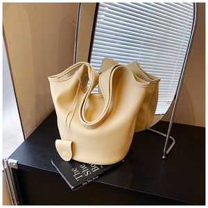 Detail of lychee pattern leather bucket bag with top handle and matching charm on dark wood