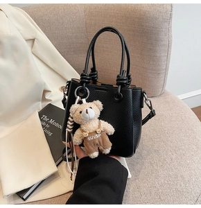 Detail of black lychee leather mini handbag with a cute teddy bear charm on a soft sofa