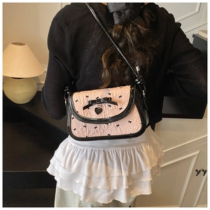 Detail of pink fabric shoulder bag with black bows and heart metal pendant accent