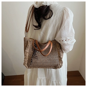 Detail of woven straw tote bag with brown leather handles and decorative silk scarf