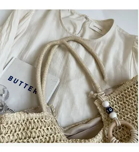Detail of woven straw tote bag with evil eye bead charm and wooden handle rings