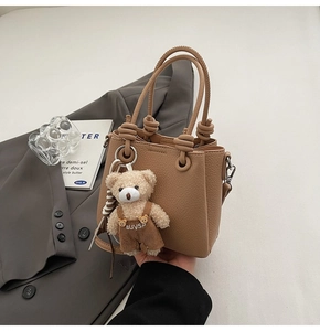 Detail of brown lychee leather handbag with knot rope handle and cute teddy bear charm